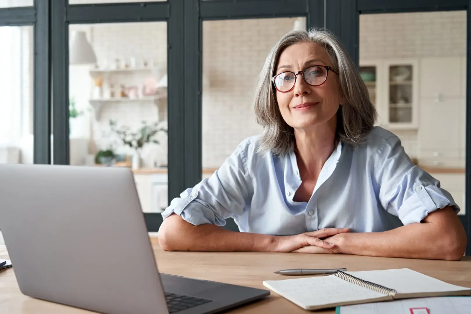 Eine ältere Frau mit grauen Haaren und brauner Brille, die lächelnd in die Kamera schaut und gerade ein Onlinecoaching absolviert.