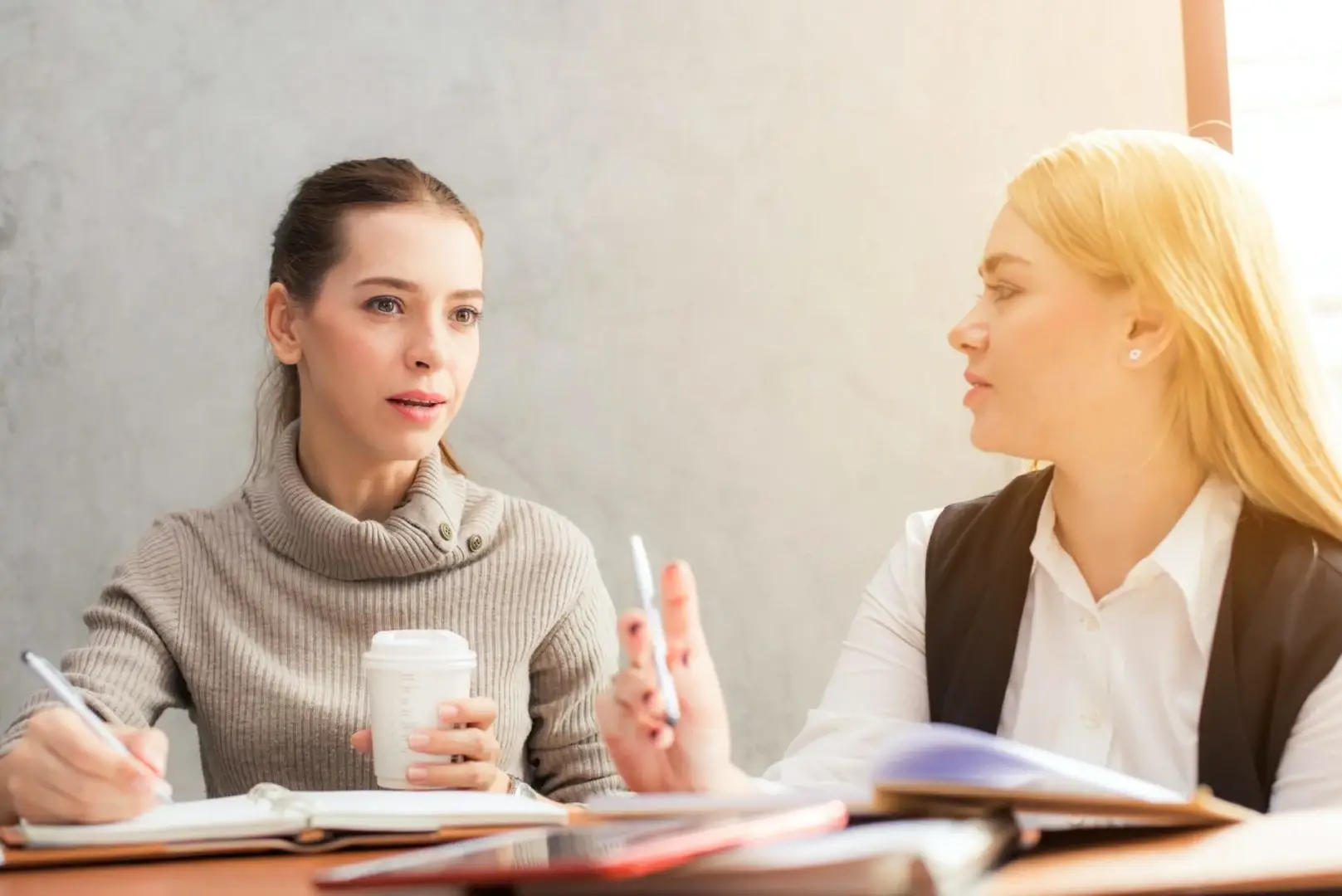 Zwei Frauen in einem professionellen Bewerbungscoaching-Gespräch, eine gibt der anderen Ratschläge und Unterstützung bei der Jobsuche in einem hellen Büro.