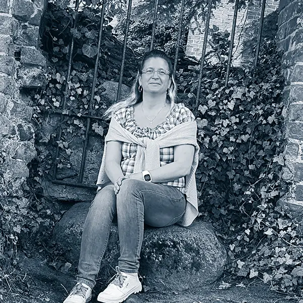 Sandra Brandt sitzt entspannt auf einem Stein im Garten, gehört zum AVGS-Coaching-Team für Gesundheit und Job.